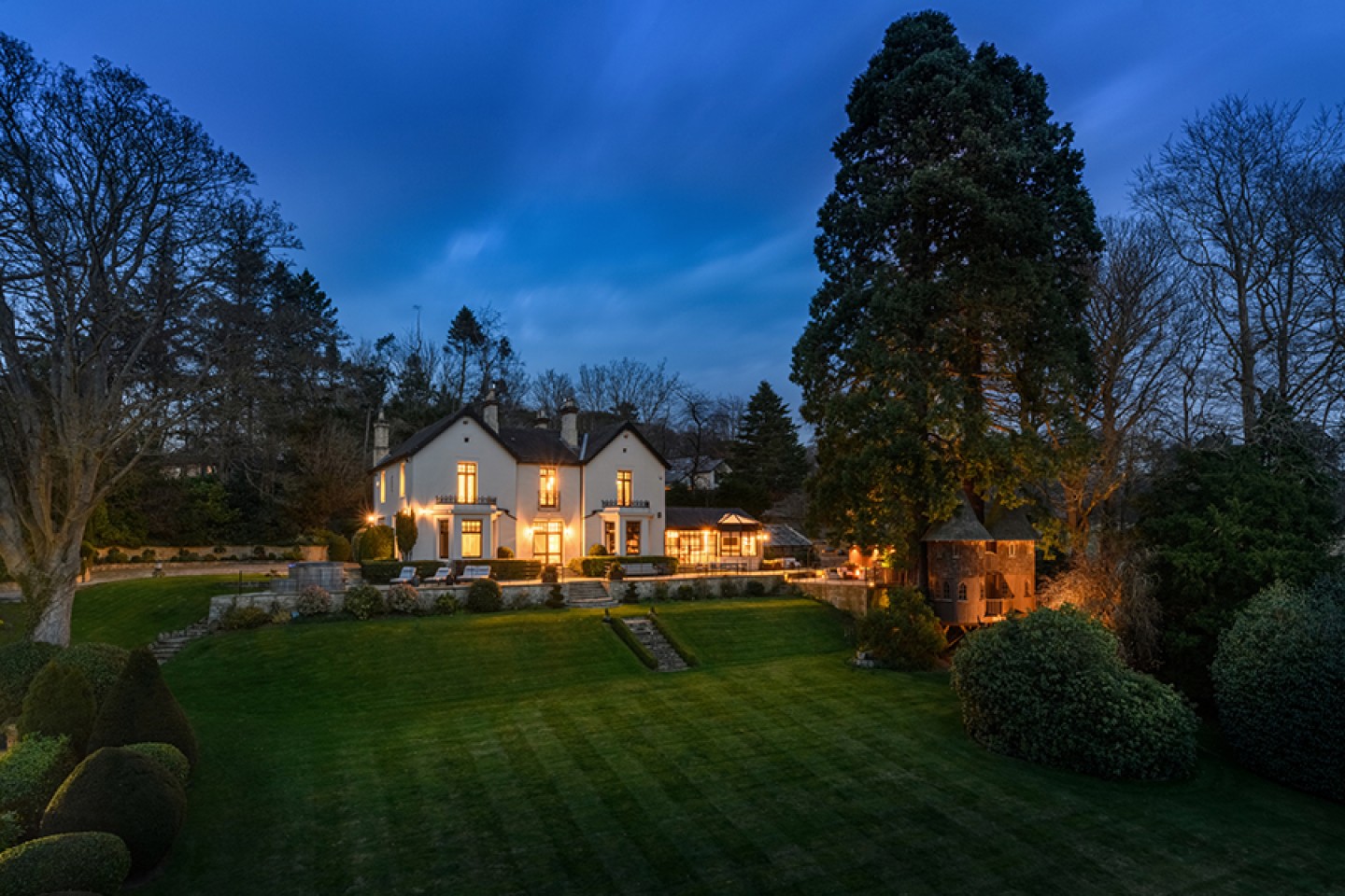 External view of the house at night, extensive lawned garden and turret treehouse
